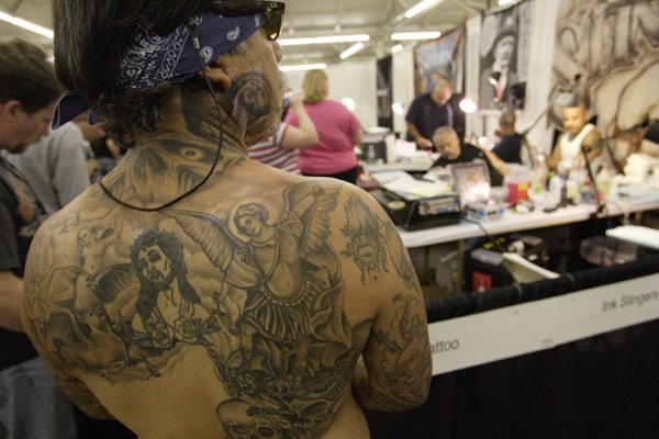 Mike Montoya watches people get tattooed as people watch him
